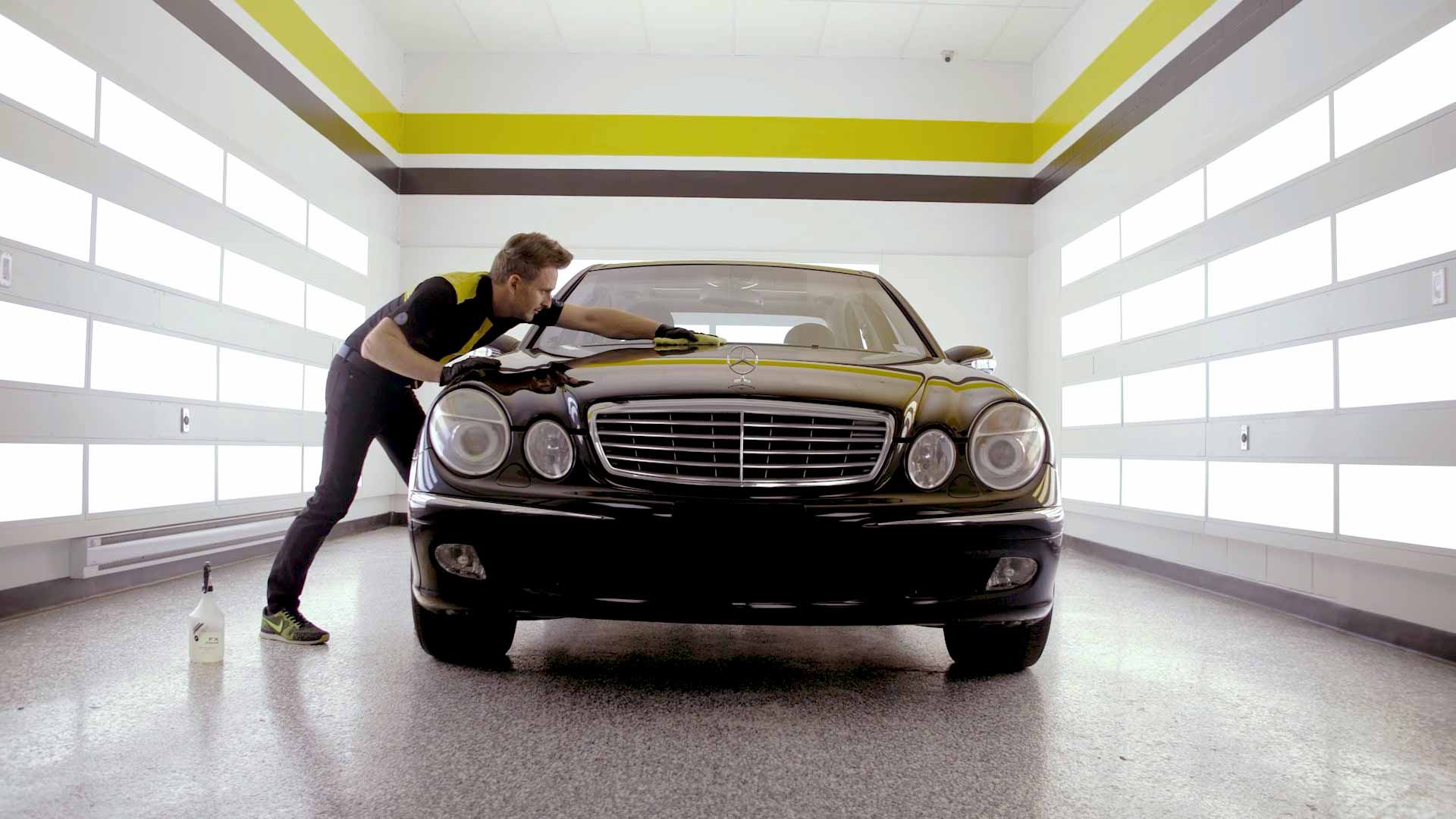 A RestorFX technician finishing the restoration of a shiny, brilliant black Mercedes lit with dramatic wall lights