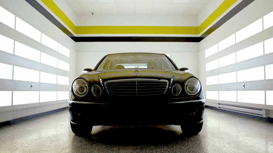 A black sedan in a RestorFX Center dramatically lit from both sides with yellow and black solid bands on high walls