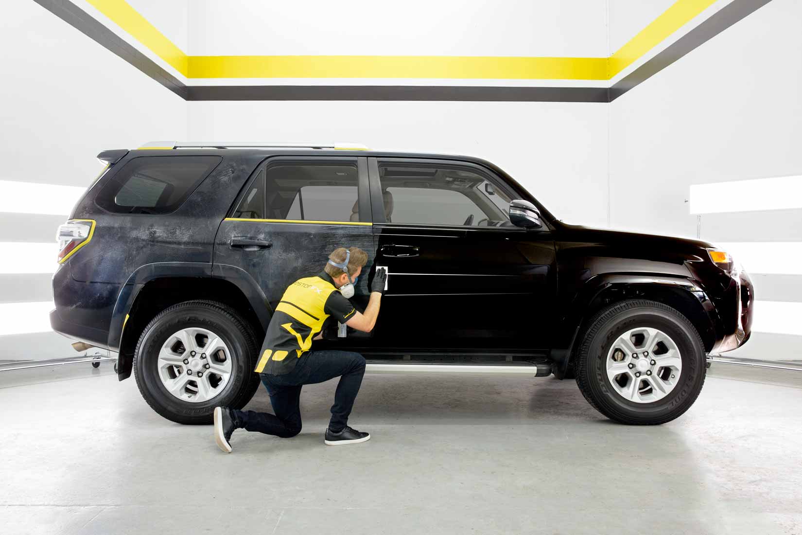 A RestorFX technician restoring the damaged and scratched side of a black SUV to a brilliant shine and luster