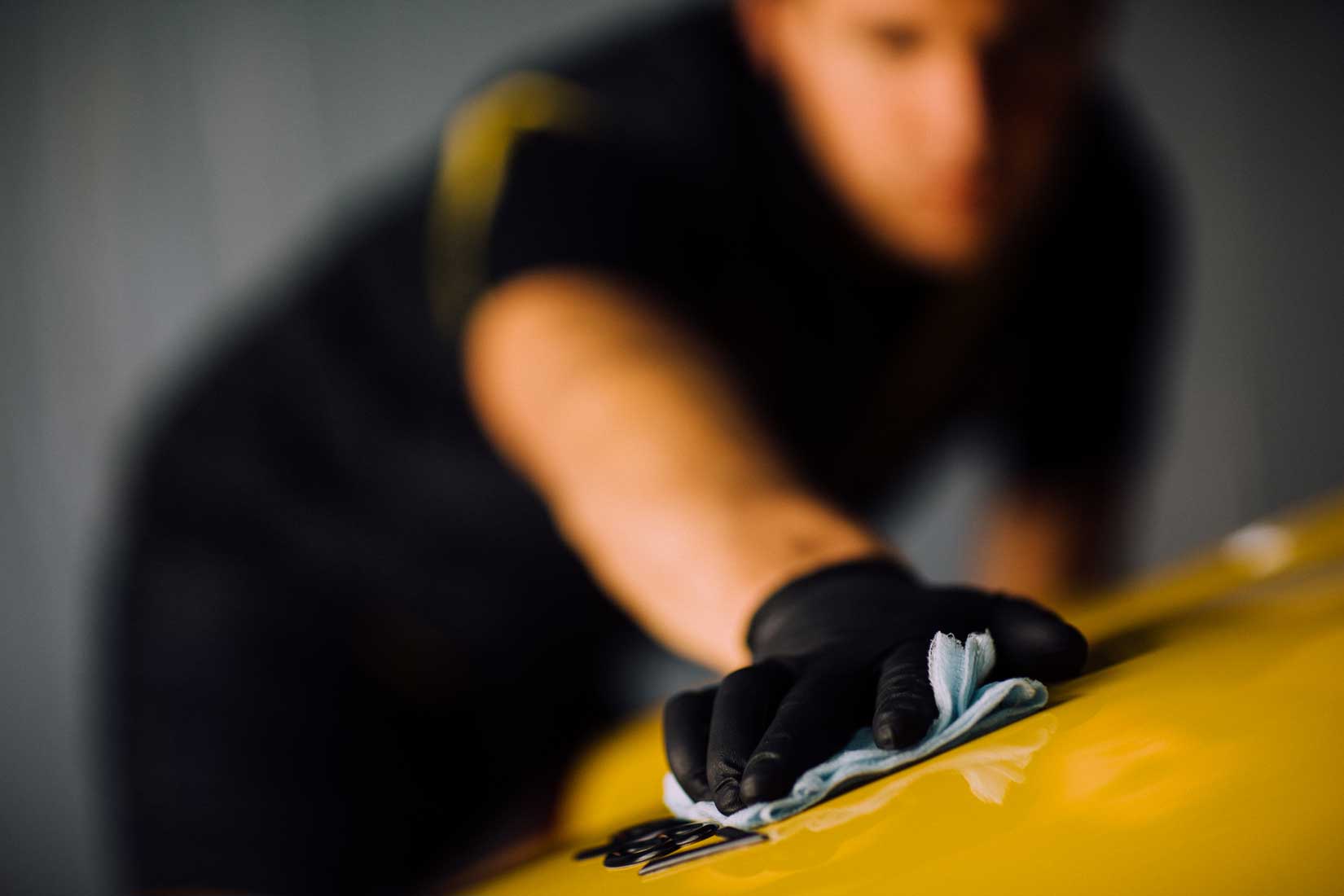 Un technicien <span  class='notranslate'>RestorFX</span> nettoie une élégante voiture de sport jaune avec un chiffon collant en vue de la restauration de la surface