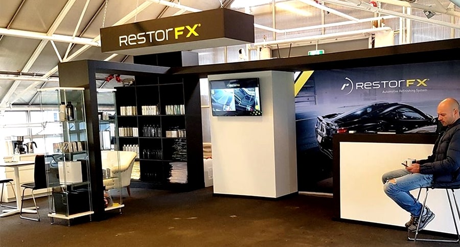 Cliente en el salón de un Centro RestorFX con pantallas, elementos de techo de marca y arte de pared de automóvil