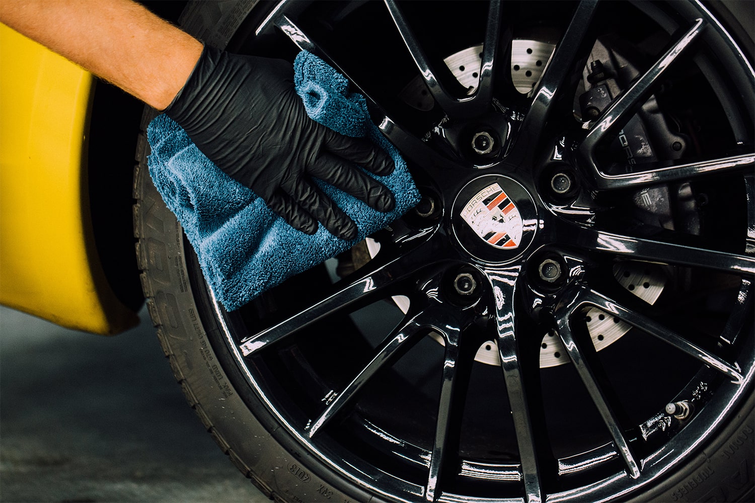 A RestorFX Technician protecting the black rim on the wheel of a yellow sports car with ClearFX Wheels product