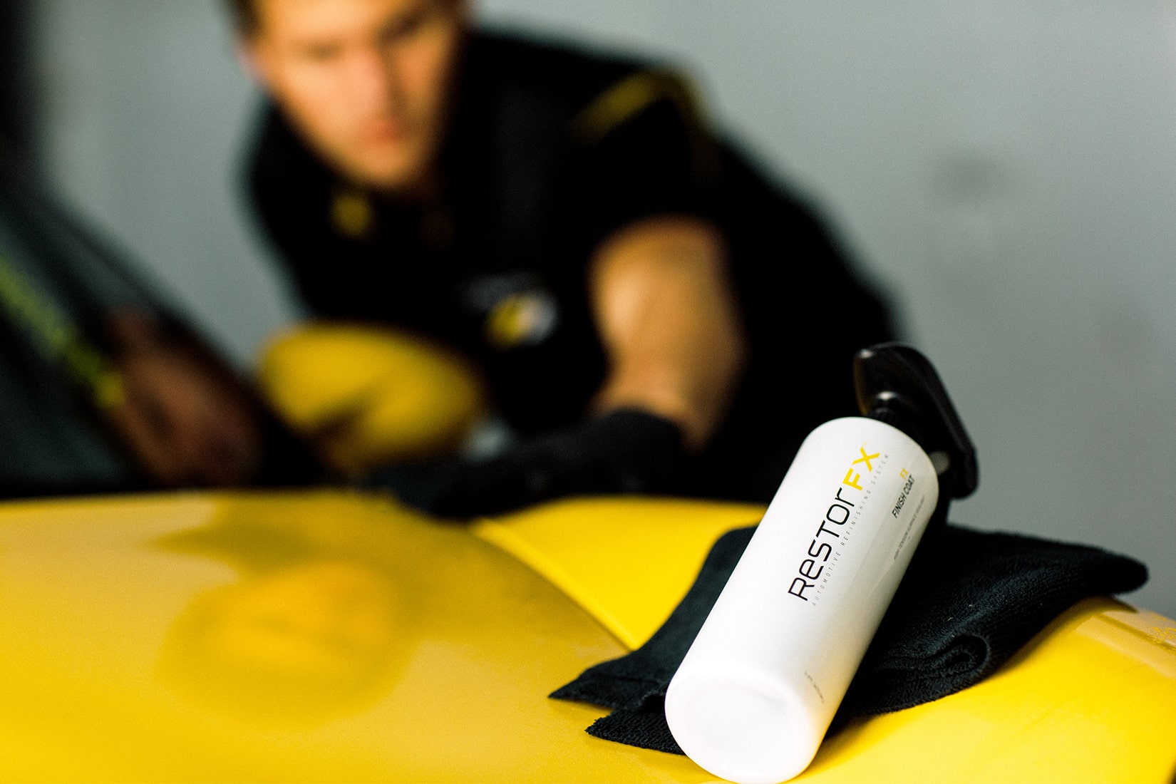 Technicien <span  class='notranslate'>RestorFX</span> travaillant de manière experte sur une élégante voiture de sport jaune avec un effet flou général