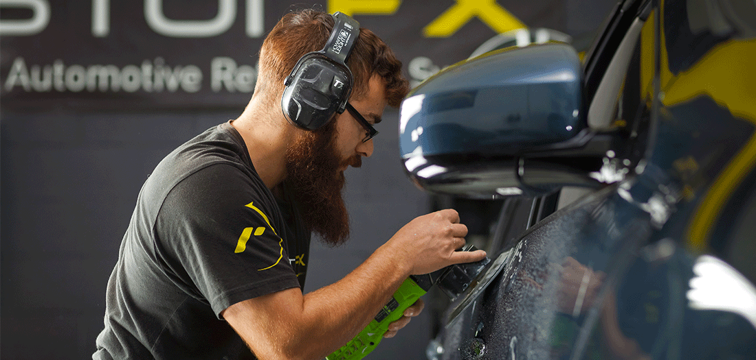  RestorFX technician in proper gear restoring the damaged and scratched surface on the side of a black sedan