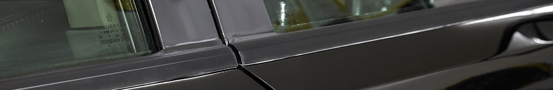 Темная, гладкая и сверкающая блестящая черная пластико-резиновая накладка на правом стекле черного автомобиля после реставрации <span  class='notranslate'>FX Trim</span> .