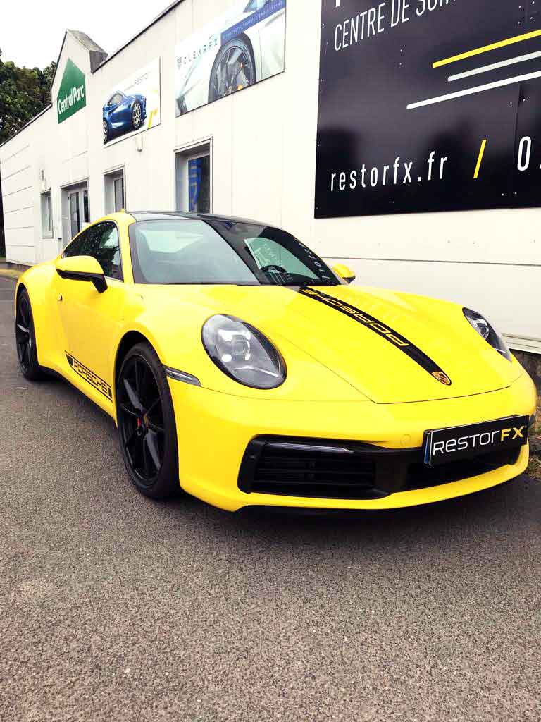 Porsche noire et jaune dans la vitrine de RestorFX Lille avec signalétique de marque et fond clair