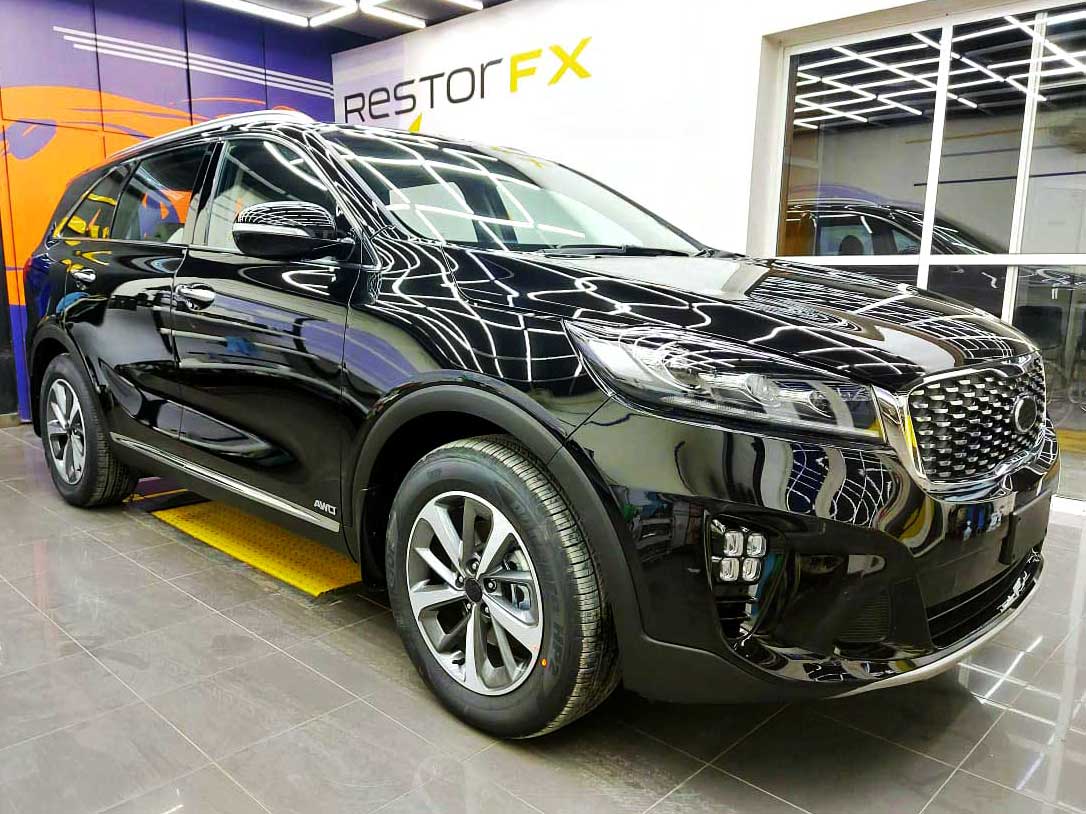 Super glossy black car at brightly lit shop area with RestorFX logo on white wall and glass windows