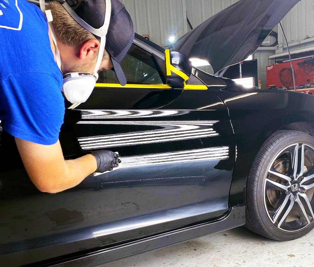 RestorFX technician applies restoration product onto brightly lit black vehicle surface area