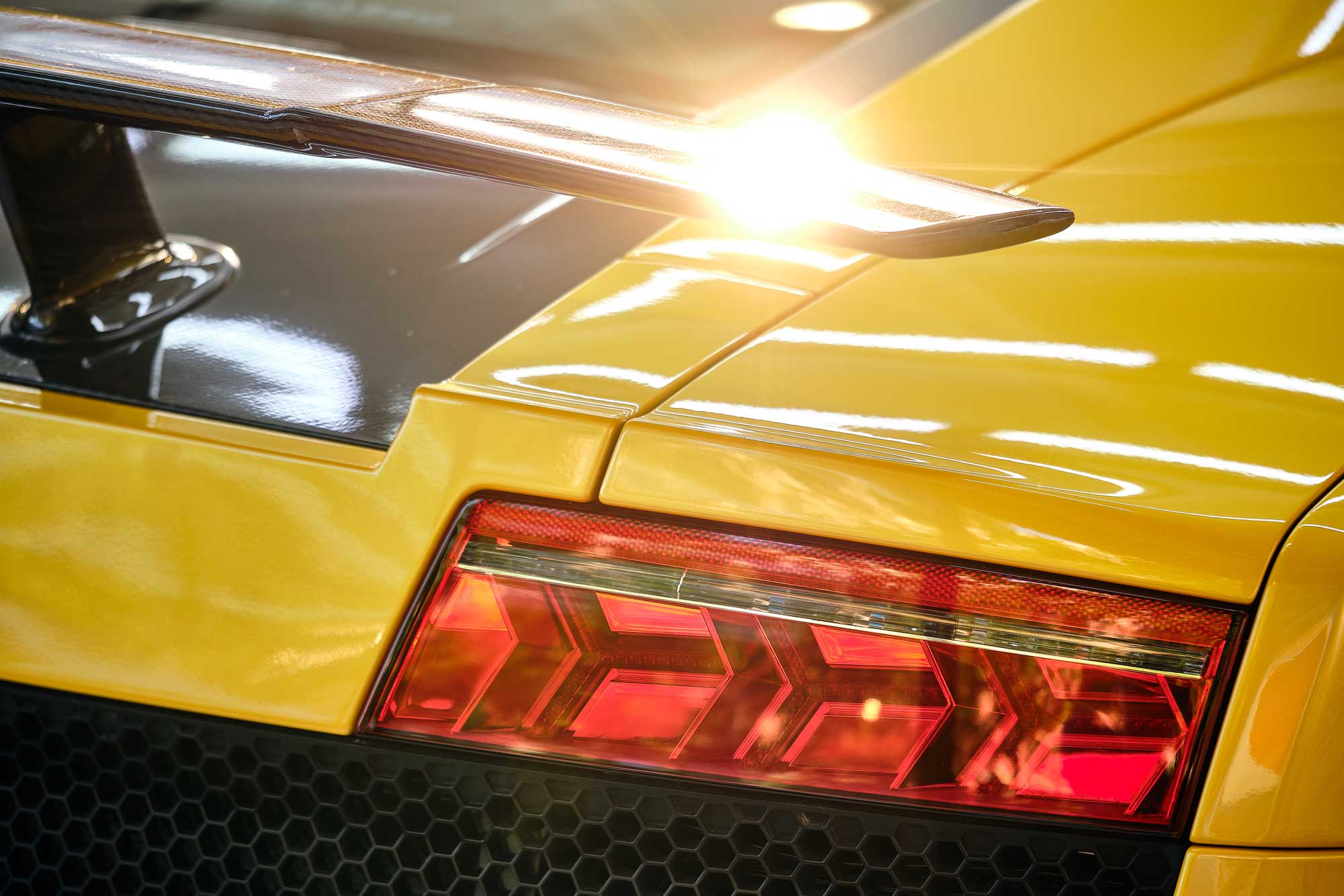 Close up rear flashlight of modern luxury yellow sportscar with sunlight reflection on spoiler