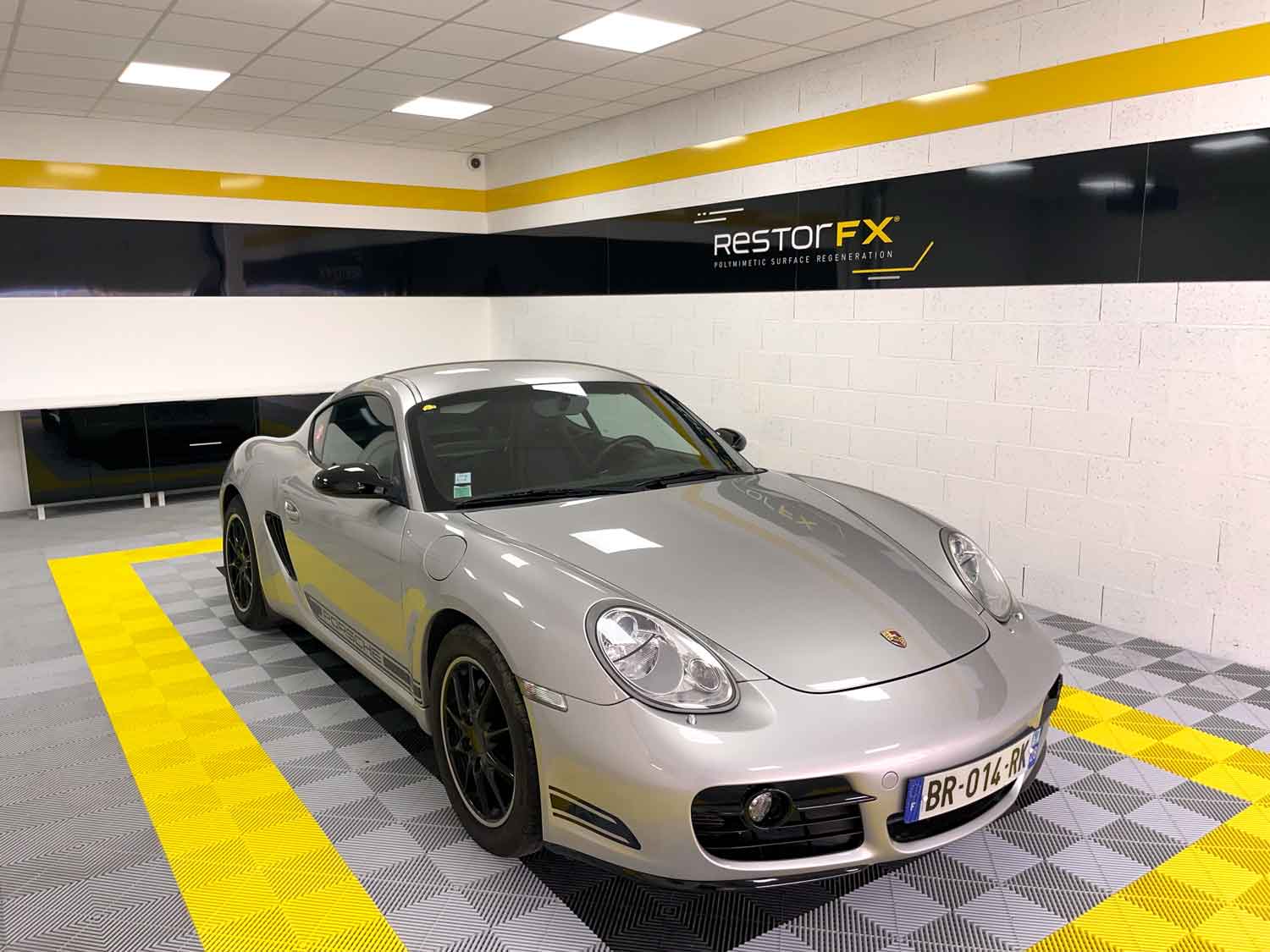 Silver Porsche at RestorFX Chartres center with branded signage and light background