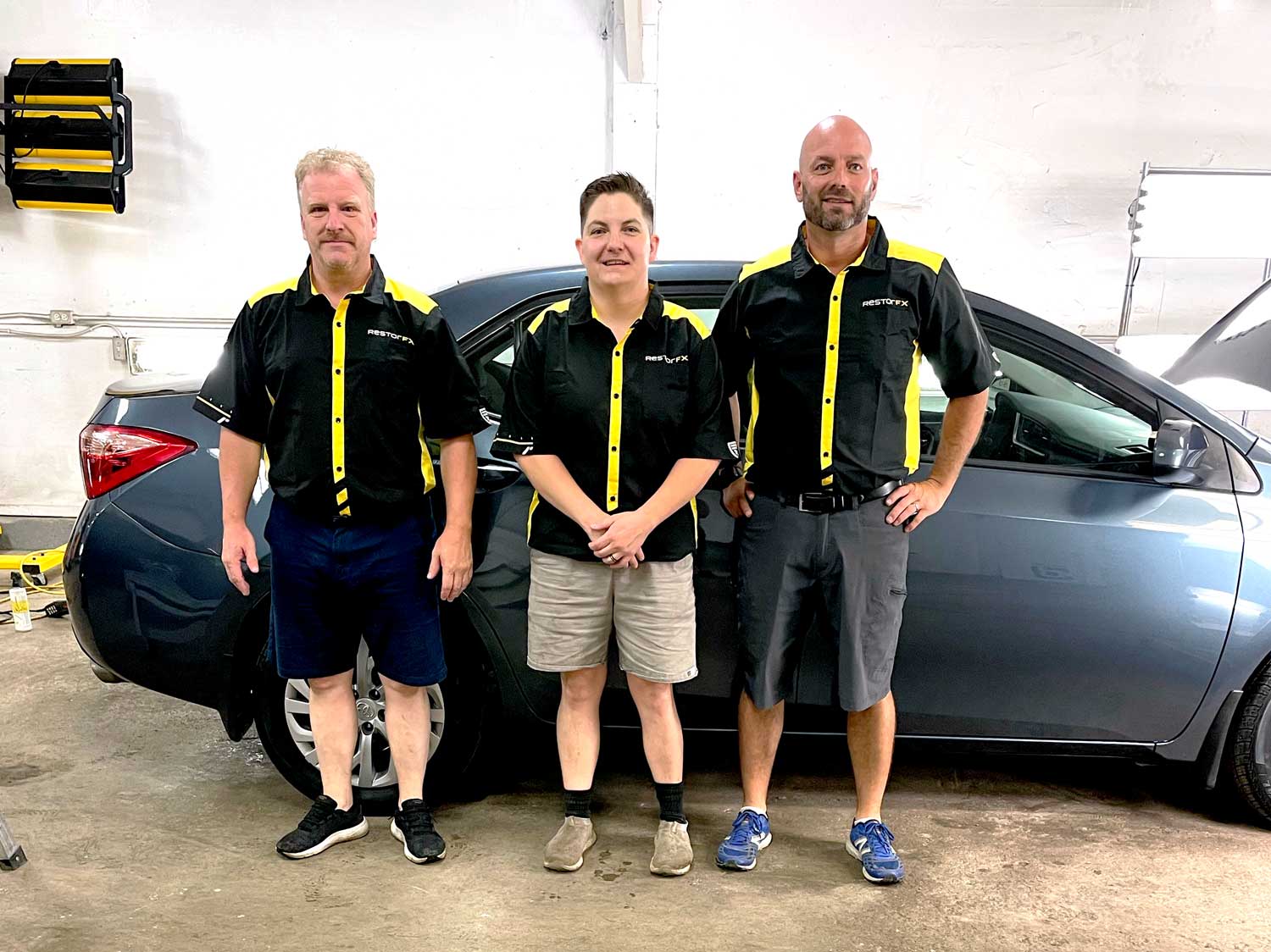 Three RestorFX Moncton staff members posing for photo in front of shiny vehicle at bright shop area