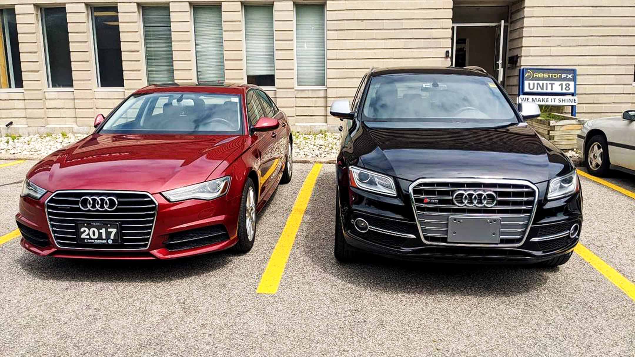Beautifully restored red Audi sedan and black Audi SUV parked in front of RestorFX Barrie