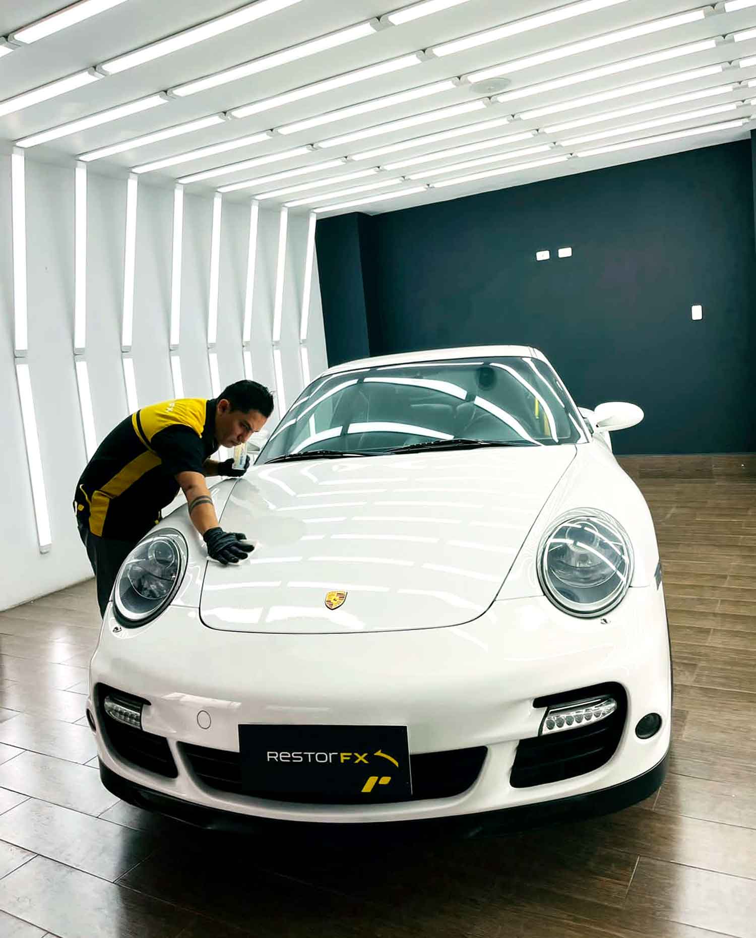 RestorFX tech applying RestorFX product on to a white Porsche parked in a well lit booth
