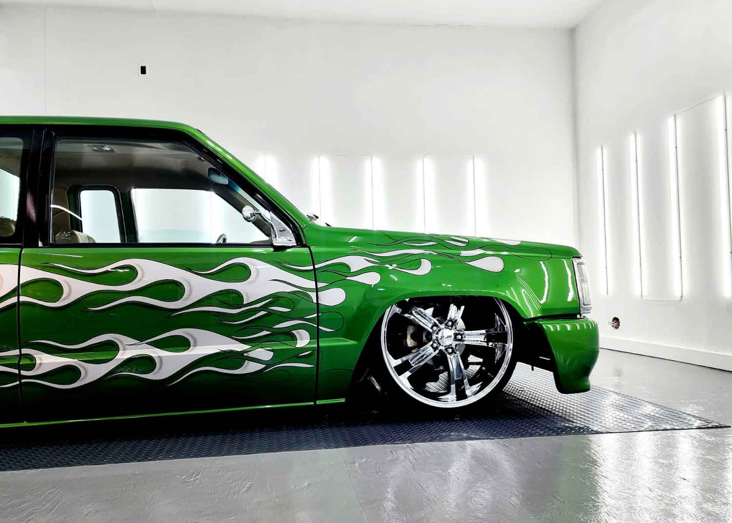 Close up of a green low rider parked in a well lit RestorFX West Niagara shop