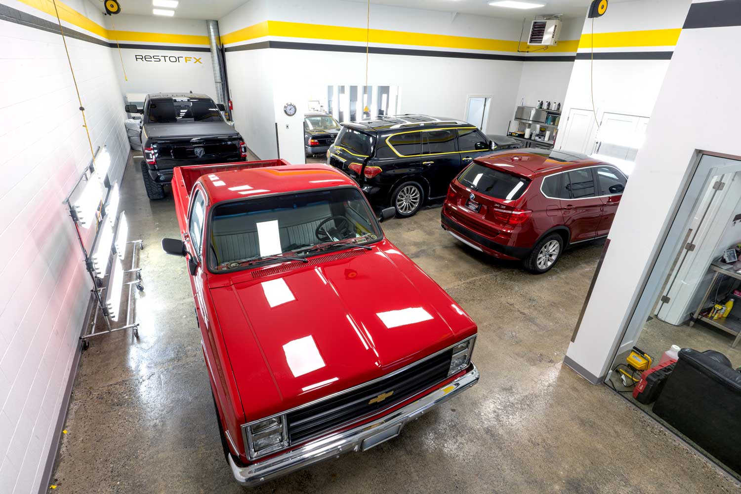RestorFX shop area with a red Chevy pickup truck, BMW X3 SUV, black Audi SUV and Ram truck