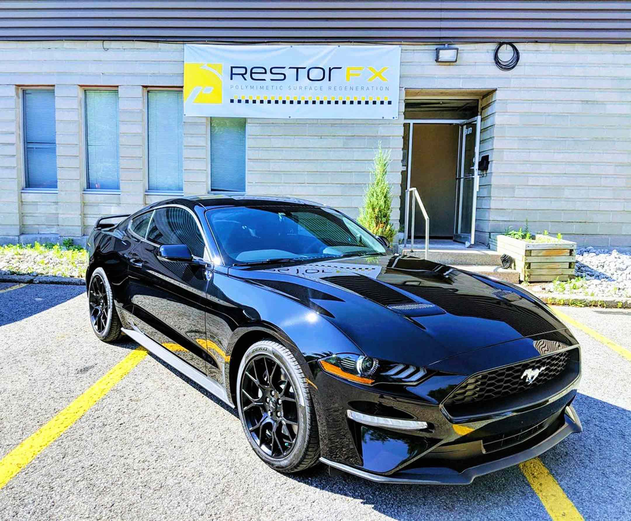 Brightly shining black Mustang outside the RestorFX Barrie storefront with grey brick walls and branded banner