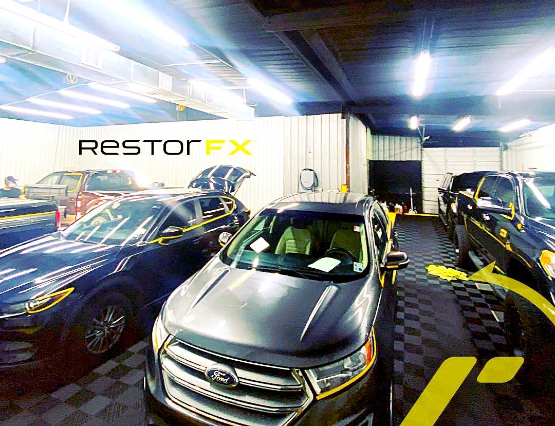 Several vehicles parked inside of RestorFX Lafayette brightly lit and branded shop area