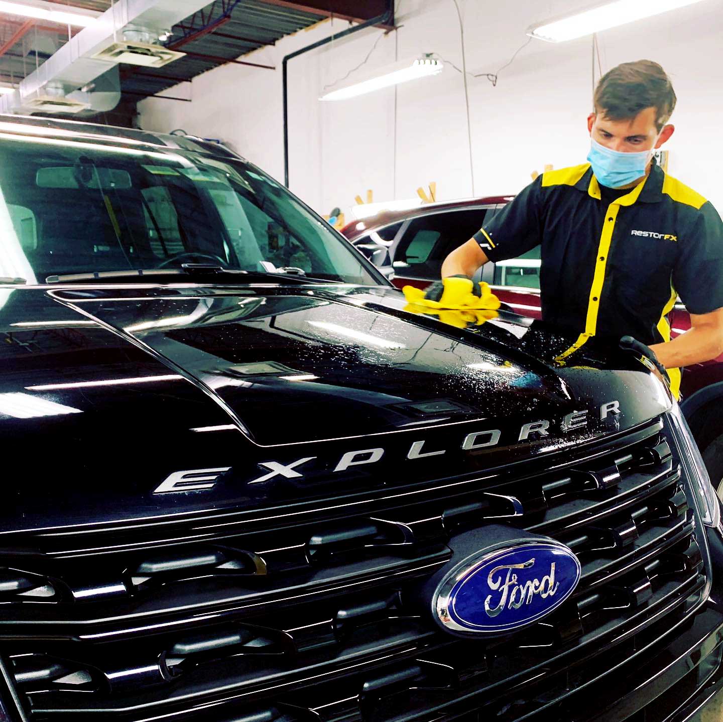 Technician wears a mask while wiping the front of black Ford Explorer during paint restoration