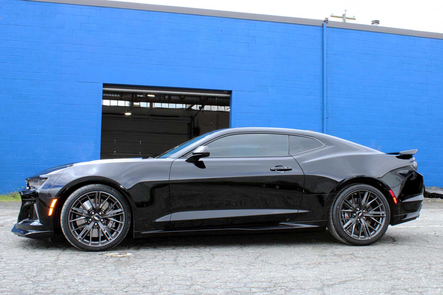 Shiny and lustered black vehicle side parked at RestorFX Richmond storefront with blue brick walls