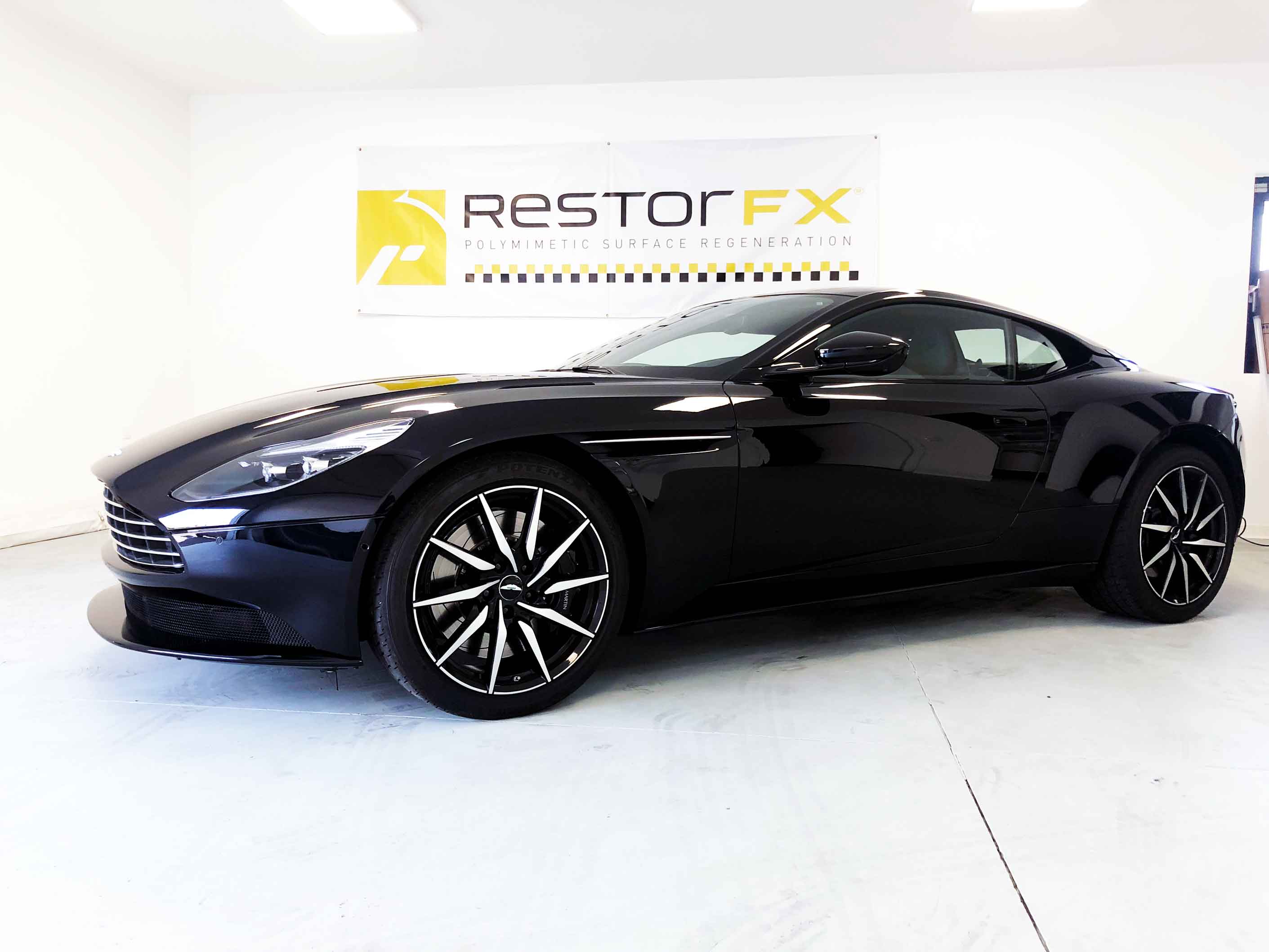 Bright black Aston Martin in highly illuminated area at RestorFX Lille with white branded walls