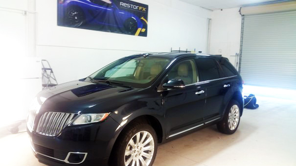 Lustered Lincoln MKX in brightly lit shop area at RestorFX Gainesville with branded signage on wall