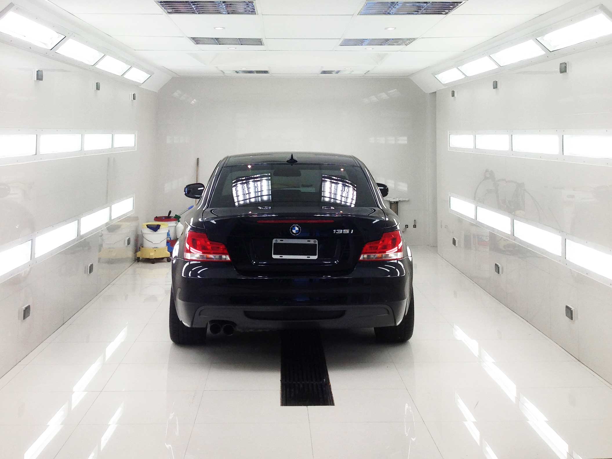 Back-view of highly glossy black BMW at the center of brightly lit cabin during restoration process