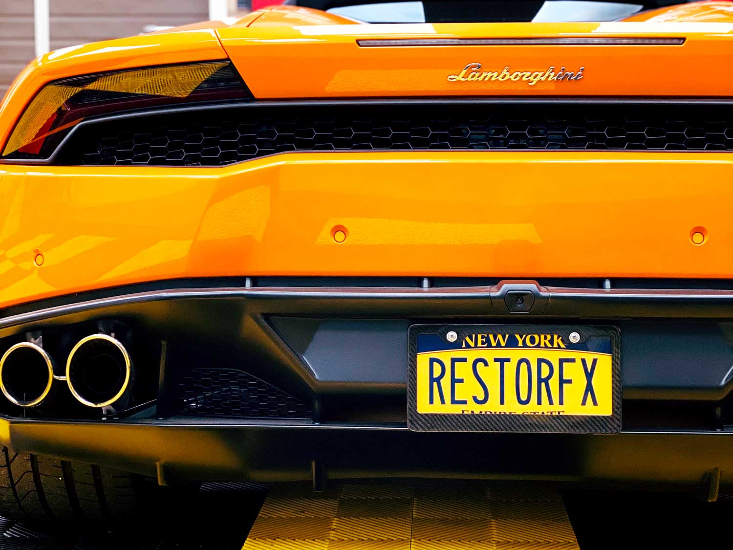 Back of glossy-finished orange Lamborghini at RestorFX Long Island shop area with custom NY plate