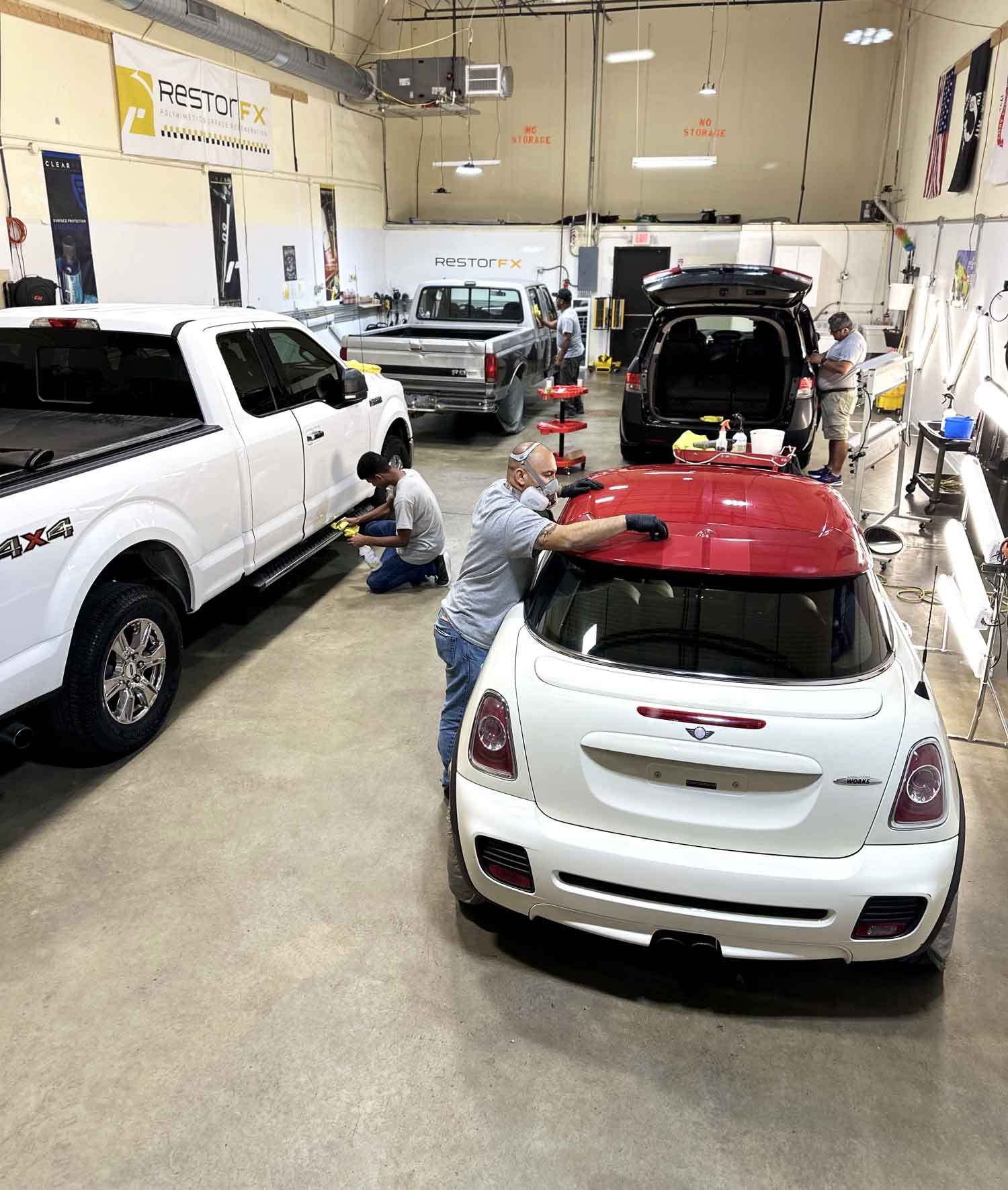 RestorFX Raleigh shop area with technicians working on a white Mini Cooper, 2 trucks and a minivan