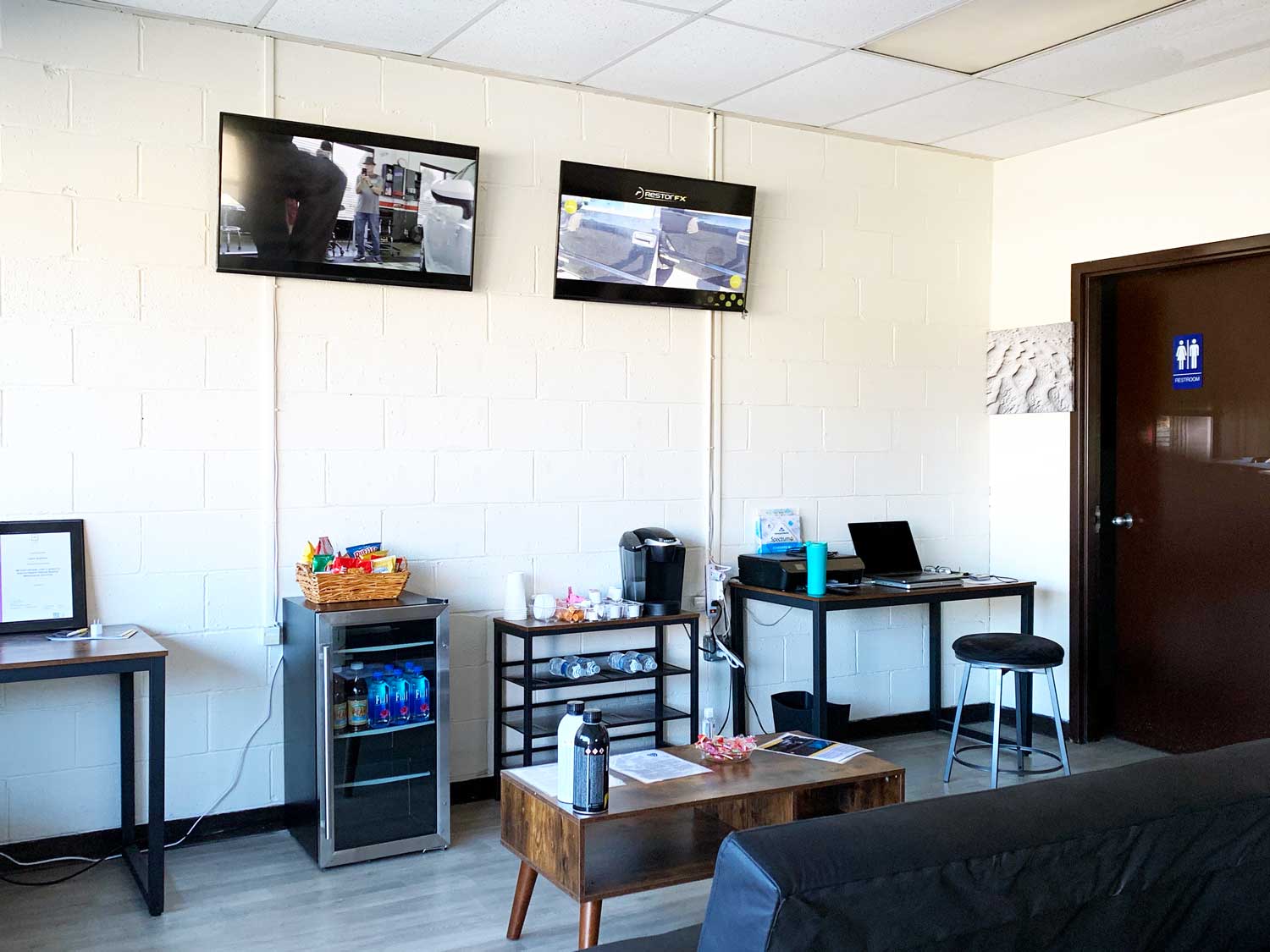 Client lounge room with white brick walls, sofa, coffee table, tv screens, desks and washroom