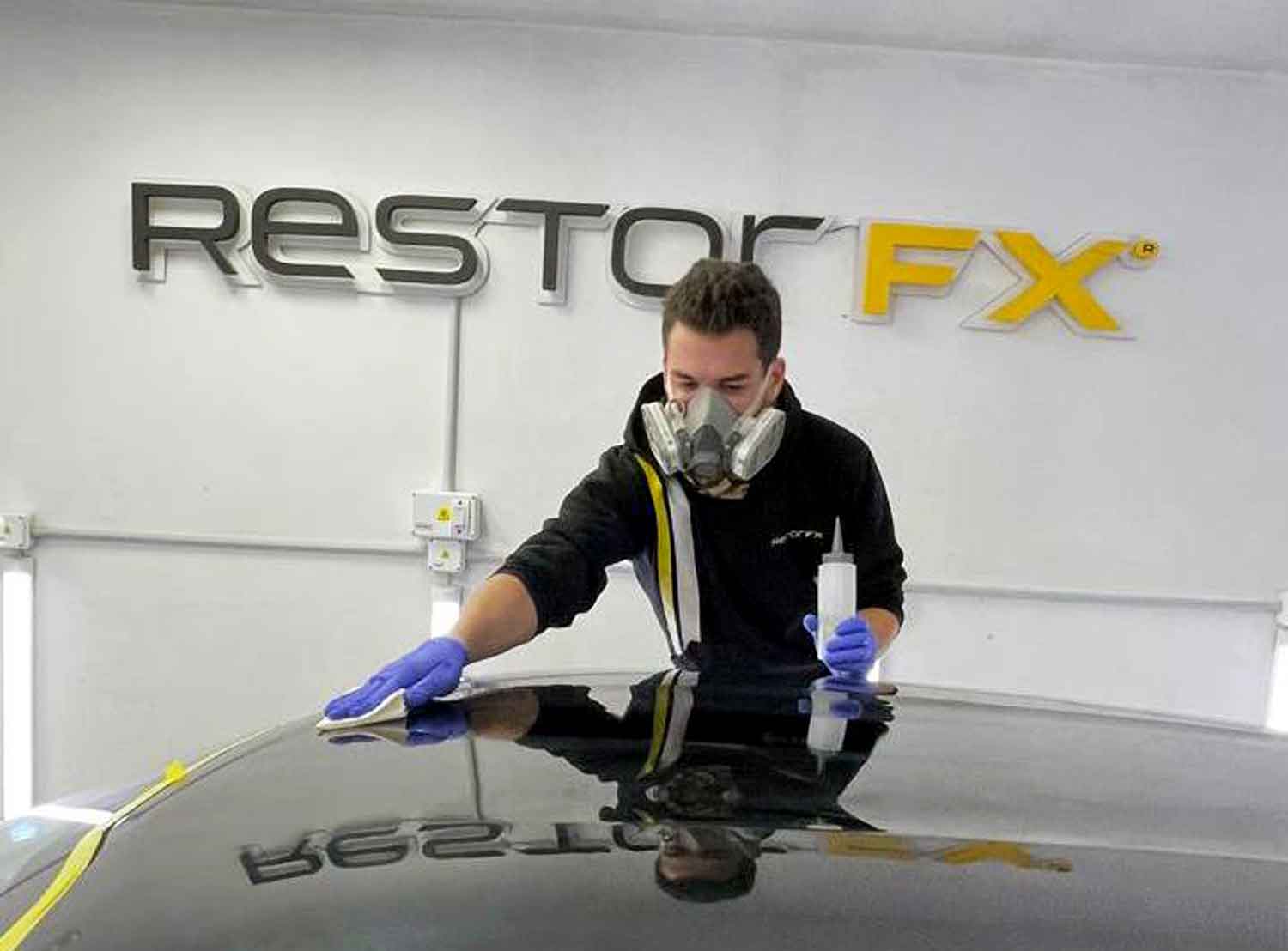 Technician applying RestorFX product onto black vehicle's surface during paint restoration process