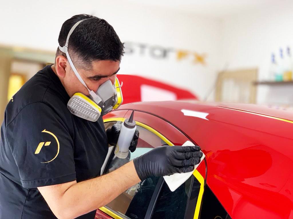 Technician applying RestorFX product onto red vehicle's surface during paint restoration process