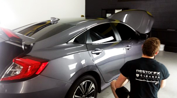 Technician kneeling next to shiny Honda with truck and hood opened up inside RestorFX shop area