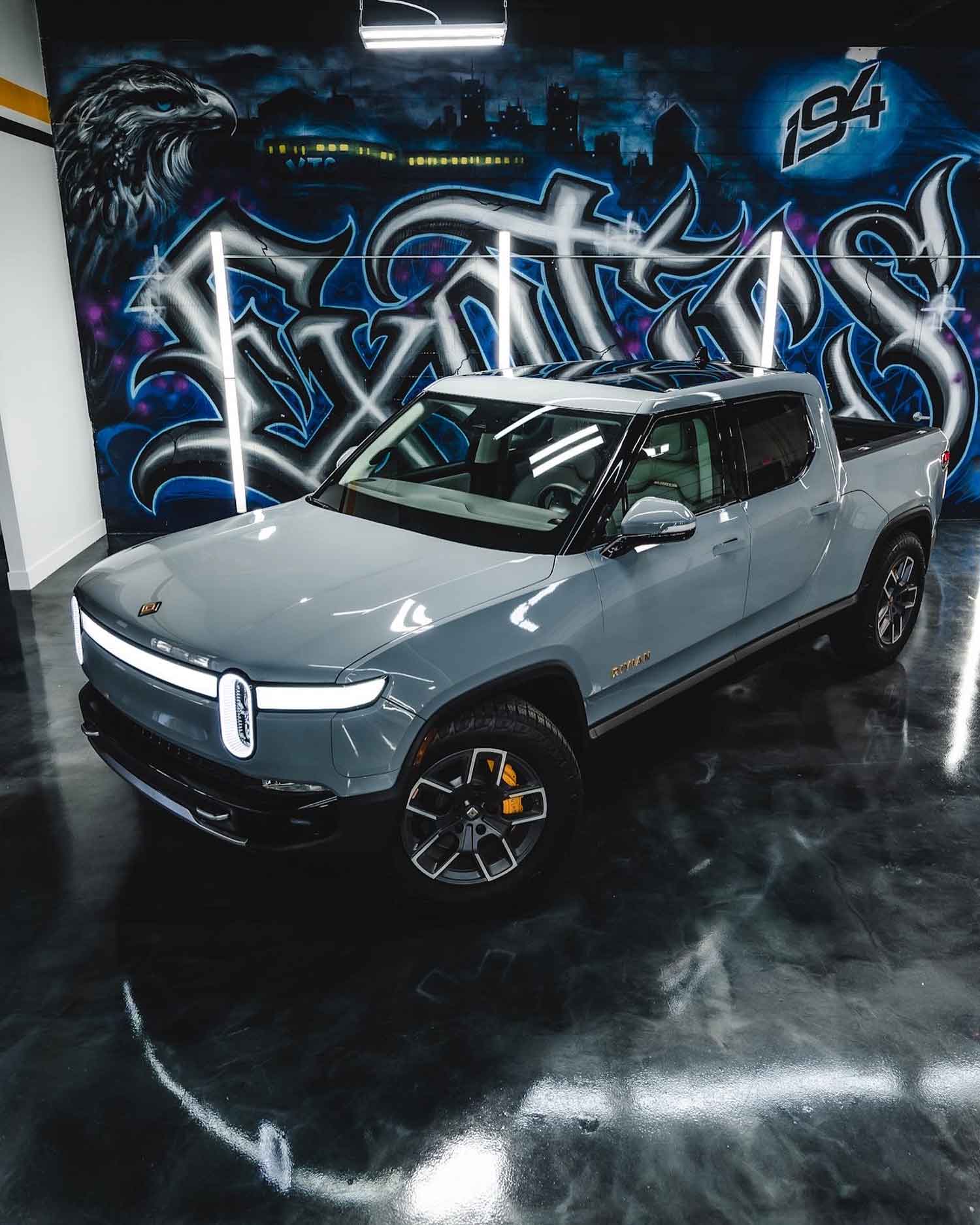 Glossy gray Rivian parked in brightly lit shop area at RestorFX Buffalo Grove with graffitied wall and black glossy floor