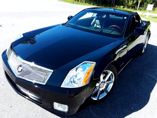 Shiny black Cadillac parked outdoors on sunny day with green vegetation in the background