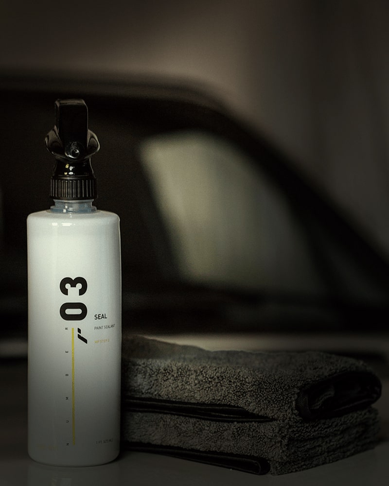 Botella de producto RestorFX Number 03 Seal y 16 Numbers Microfiber con un coche al fondo