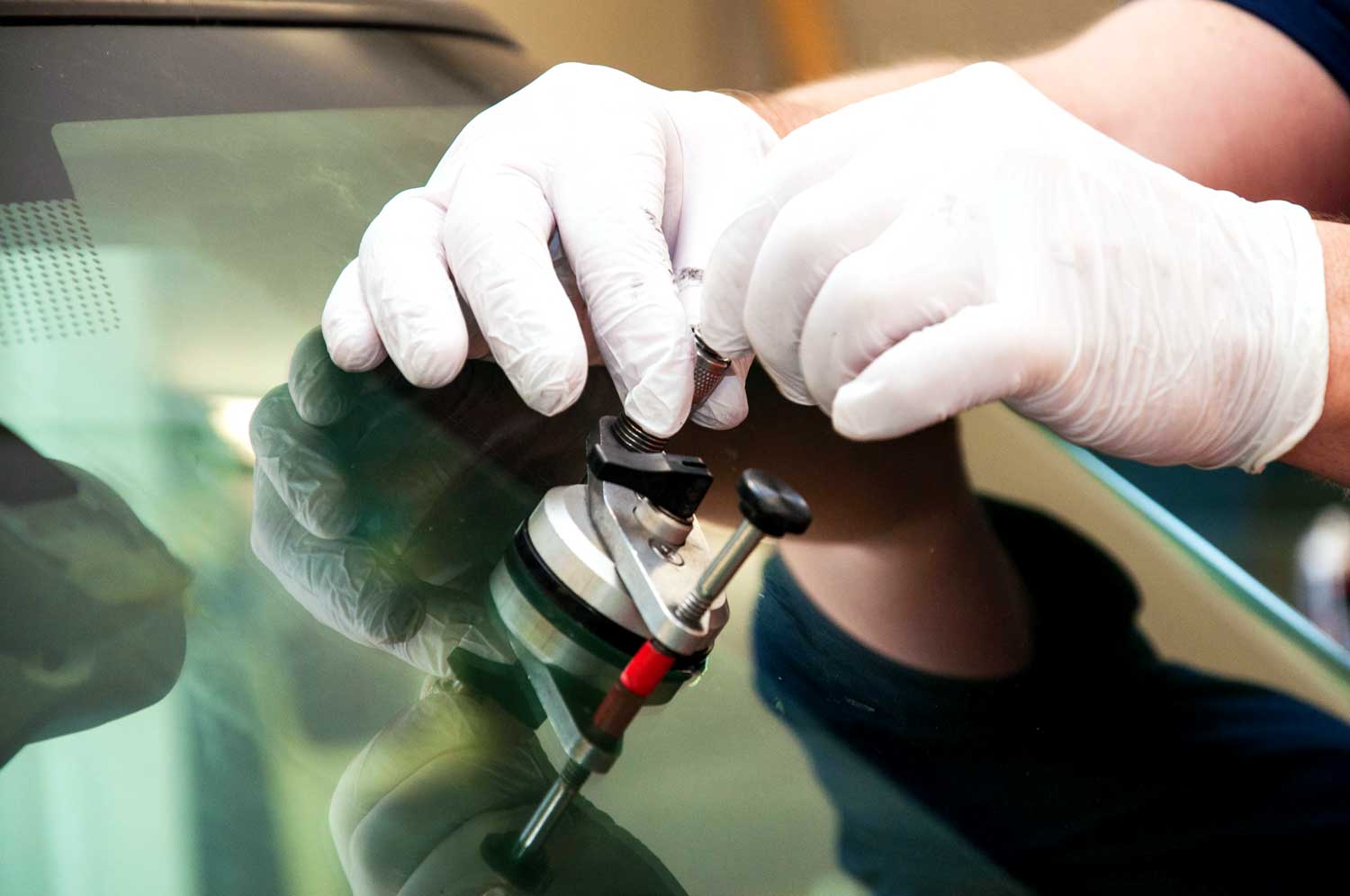 Un technicien ganté réparant des éclats de roche sur le pare-brise à l'aide d'un outil de réparation d'éclats de verre