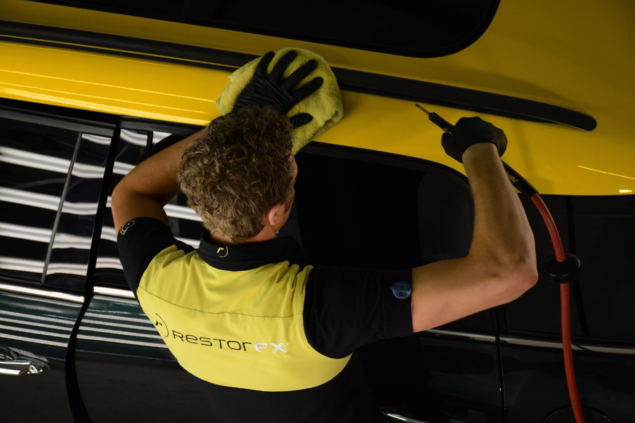 Un technicien <span  class='notranslate'>RestorFX</span> utilisant de l'air comprimé pour sécher les crevasses et la surface d'un véhicule jaune pour le traitement <span  class='notranslate'>RestorFX</span>