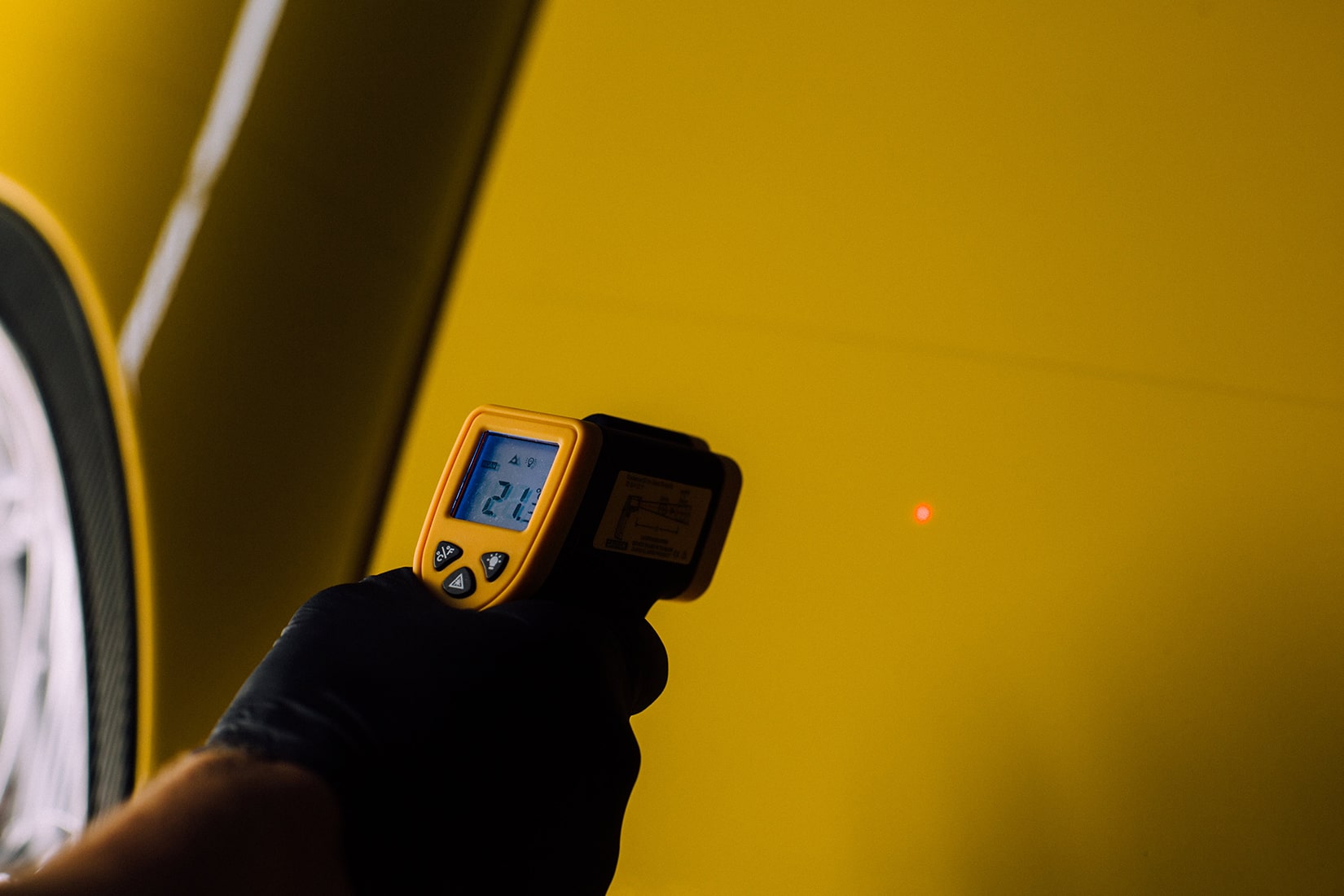 Техник <span  class='notranslate'>RestorFX</span> проверяет температуру поверхности желтого спортивного автомобиля с помощью цифрового инфракрасного термометра.