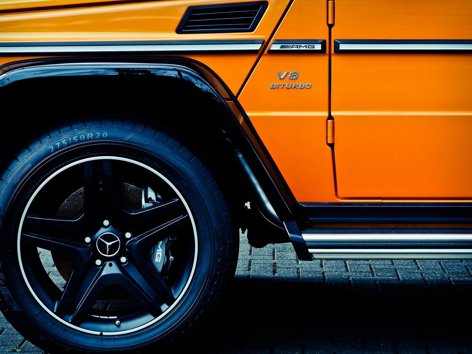 オレンジ色の SUV の印象的な黒い左前輪、鮮やかな部分ドア、光沢のあるシルバーのランニング ボード