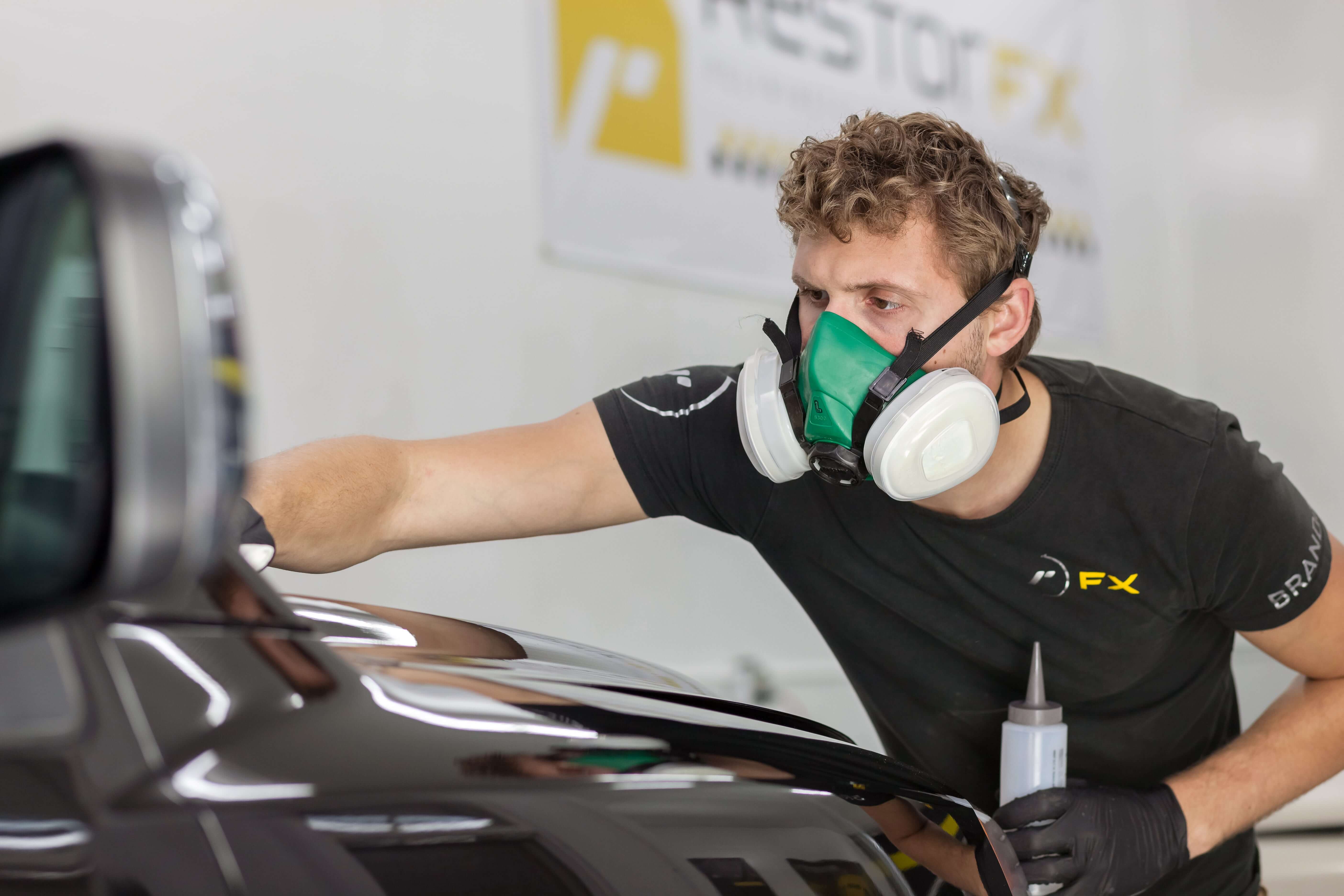 Um técnico <span  class='notranslate'>RestorFX</span> usando uma máscara restaurando quimicamente a superfície de pintura danificada de um veículo