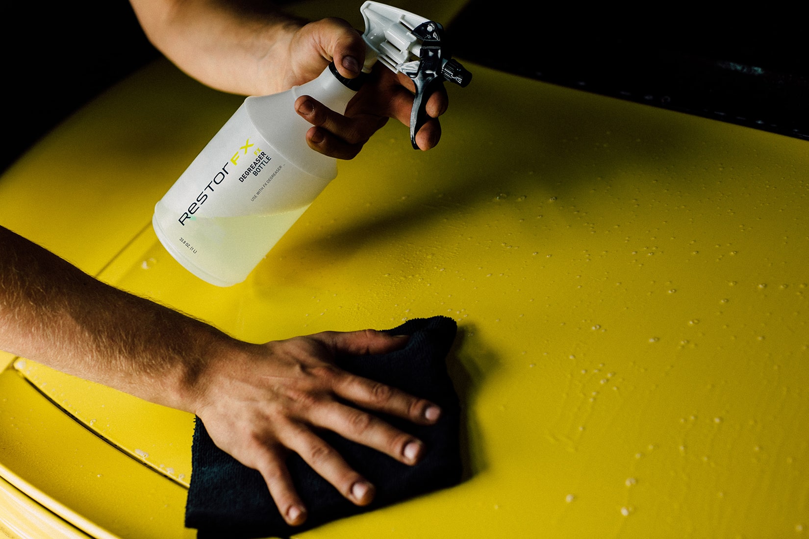 A RestorFX technician spraying and wiping the surface of a yellow sports car with FX Degreaser