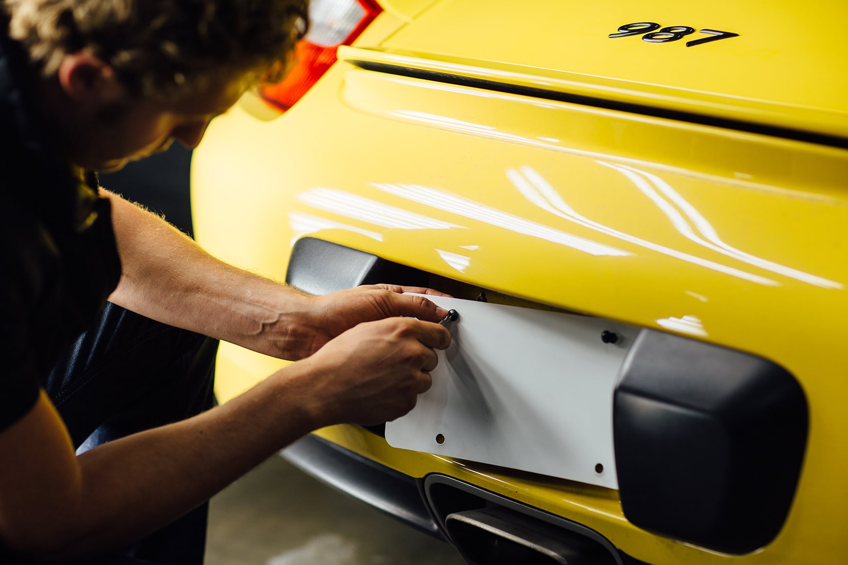 Un técnico de  RestorFX  desatornillando las placas de un auto deportivo amarillo
