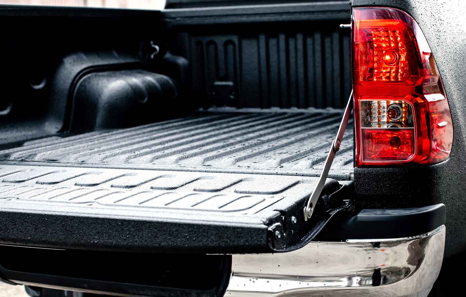 Black spray-on bedliner of a black car with a chrome bumper