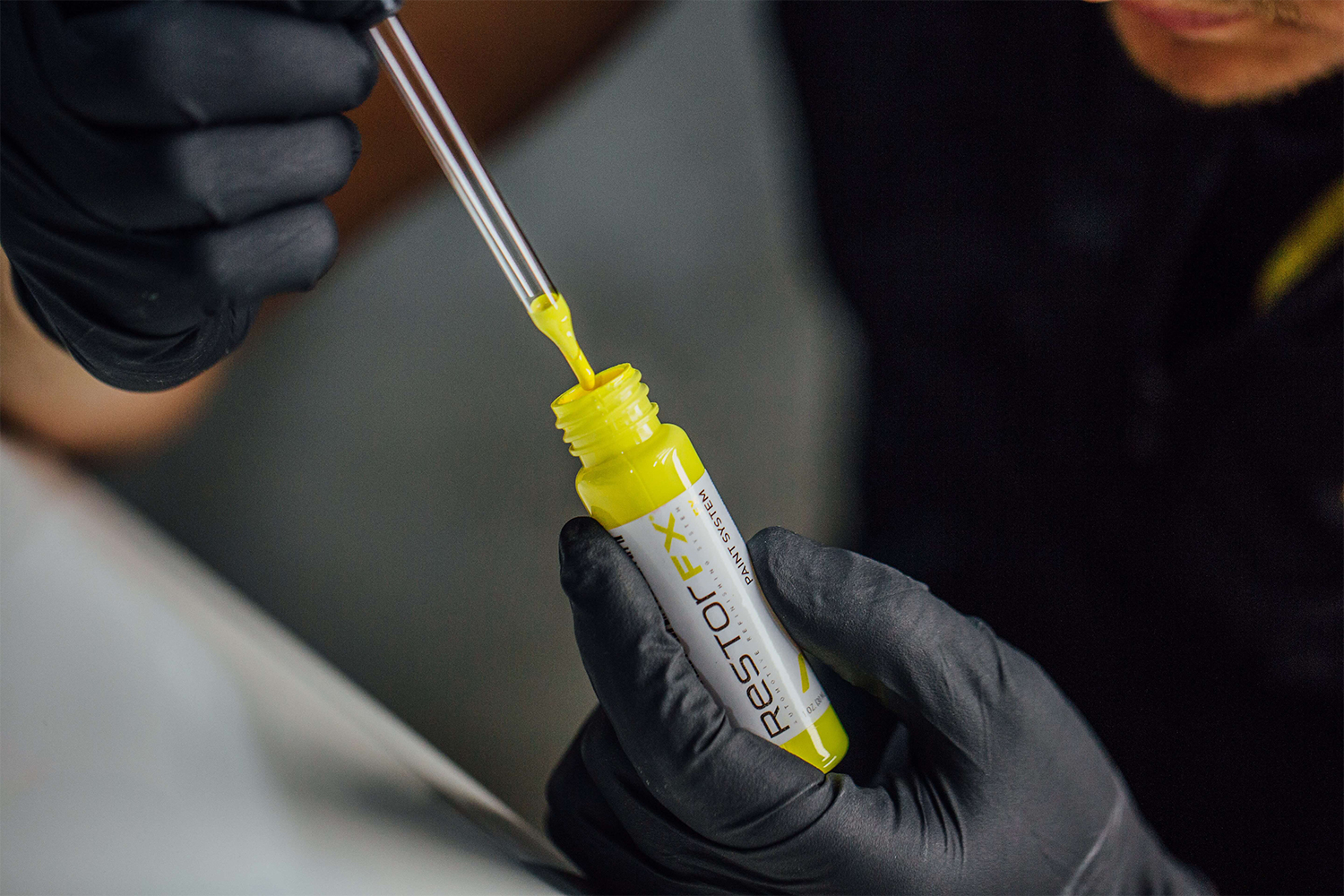 The gloved hands of a RestorFX Technician extracting yellow paint from a RestorFX Paint vial for paint chip repair