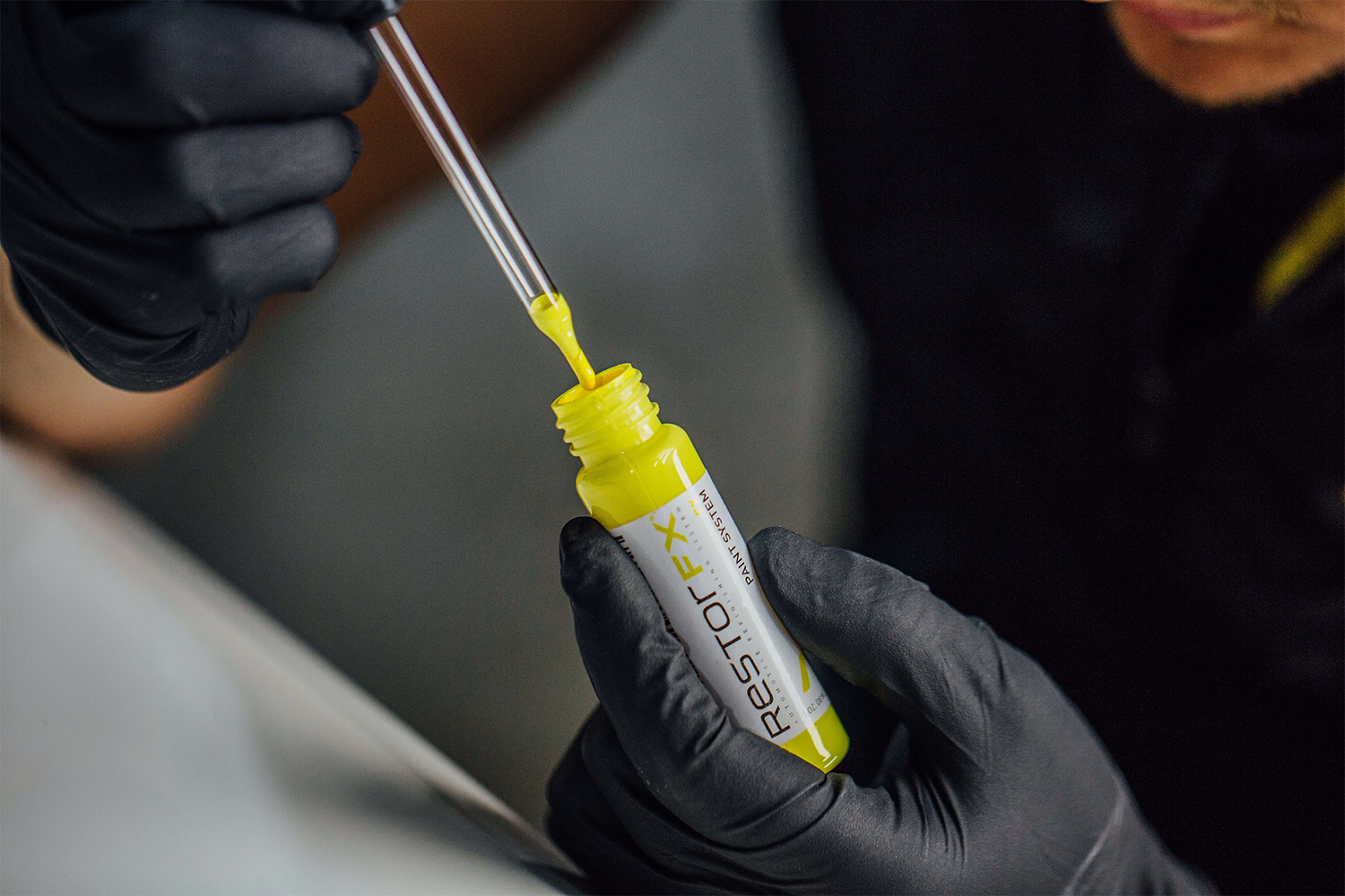 Les mains gantées d'un technicien RestorFX extrayant de la peinture jaune d'un flacon de peinture RestorFX pour la réparation des éclats de peinture