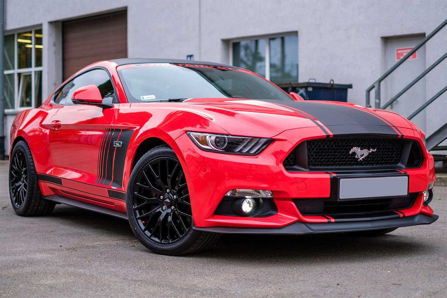 Front of a shiny, pristine red car showing its brilliant black grill and trim around the plate and bumper