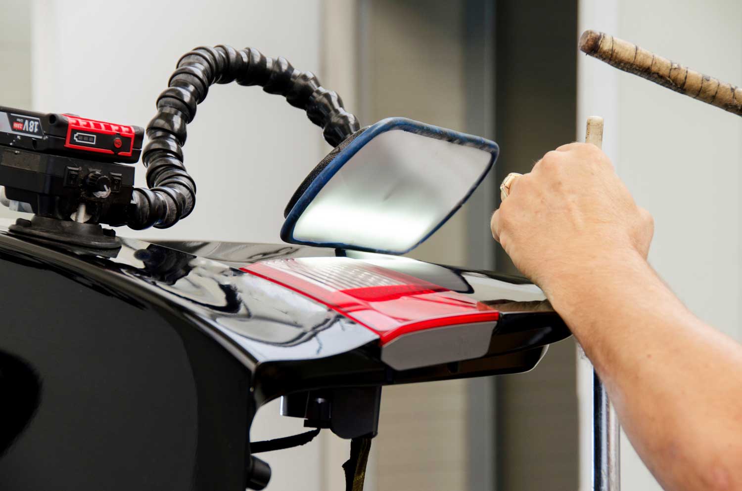 An automotive paint technician repairing dents on a black vehicle panel without having to repaint