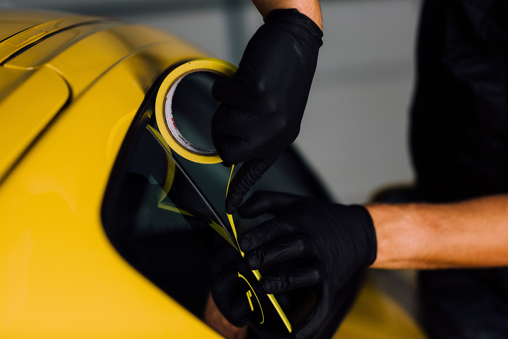 Un técnico de  RestorFX  quitando la moldura de la ventana de un auto deportivo amarillo para preparar el vehículo para la restauración de la pintura