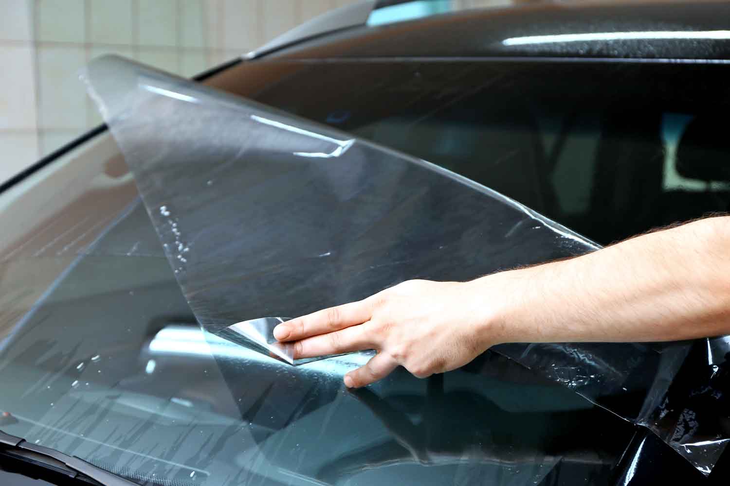 Technician applying clear protection film to the windshield of a black car