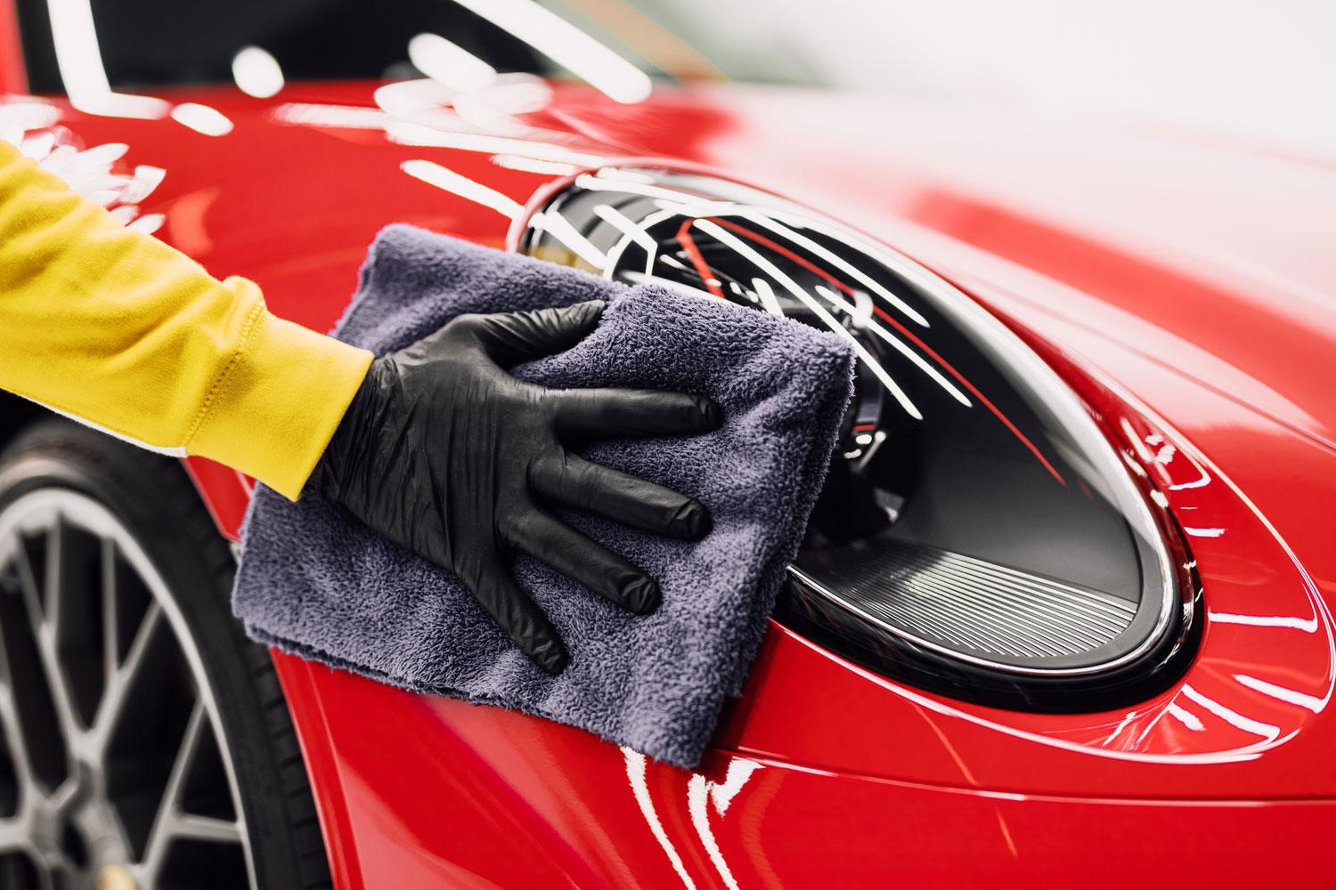 A technician wiping the headlight of a red sports car with a microfiber towel